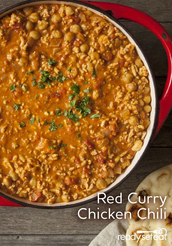 a red pot filled with chicken chili next to pita bread on a wooden table