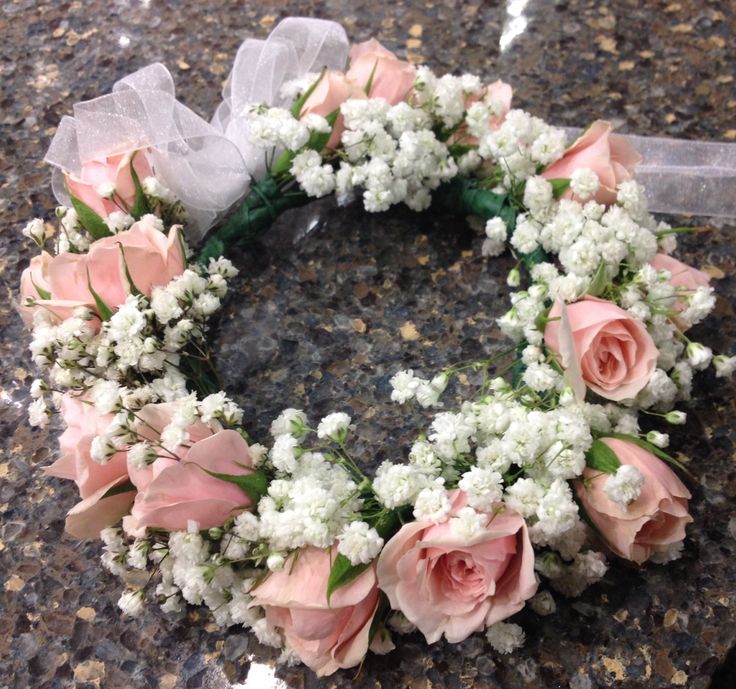 a wreath with pink roses and white baby's breath is on the ground in front of a stone wall