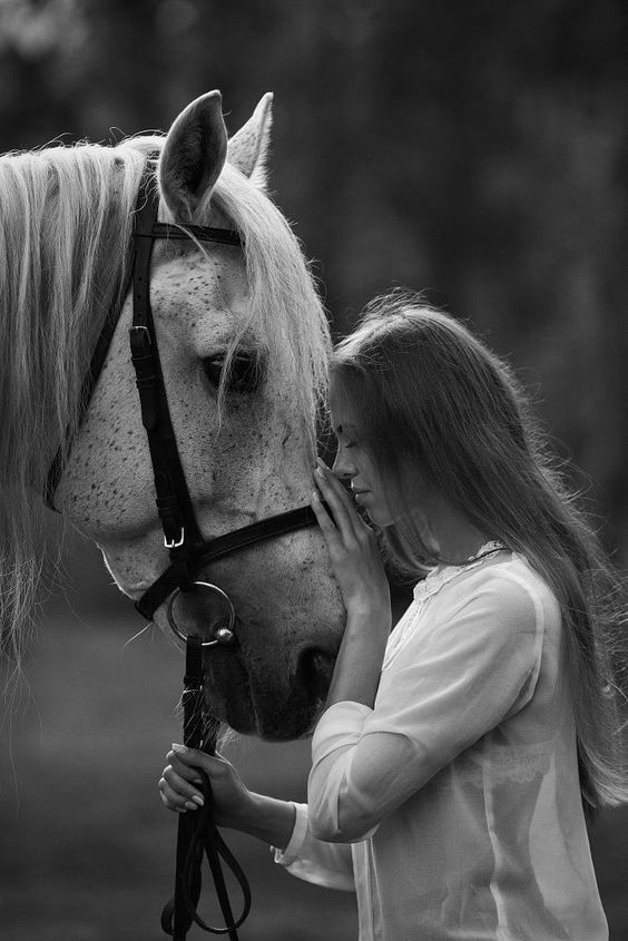 a woman standing next to a horse while holding the bridle on it's head