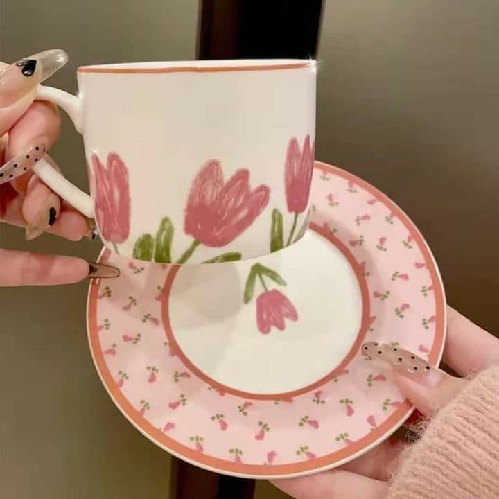 a woman holding a cup and saucer with pink flowers on the rim, in front of a mirror