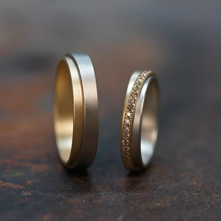 two gold wedding bands with white and yellow diamonds set in them on top of a table