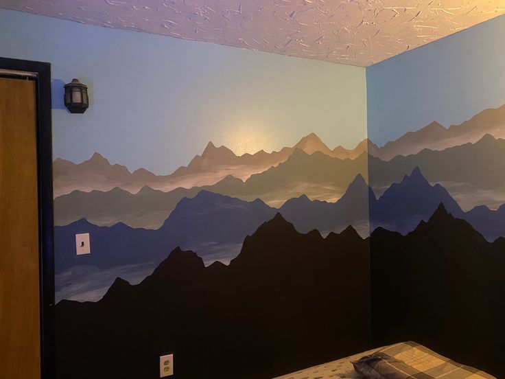 a room with mountains painted on the wall and a bed in front of it,