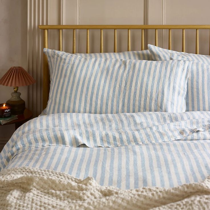 a bed with blue and white striped sheets on top of it next to a night stand