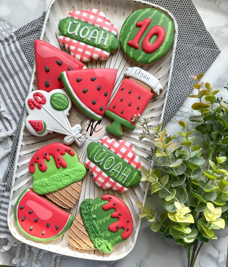 decorated cookies in the shape of watermelon and ice cream on a plate next to flowers