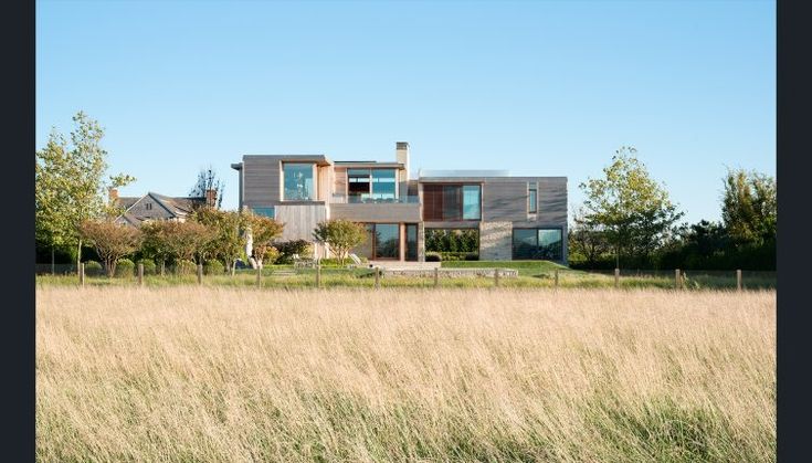 a large house sitting on top of a lush green hillside next to tall grass and trees