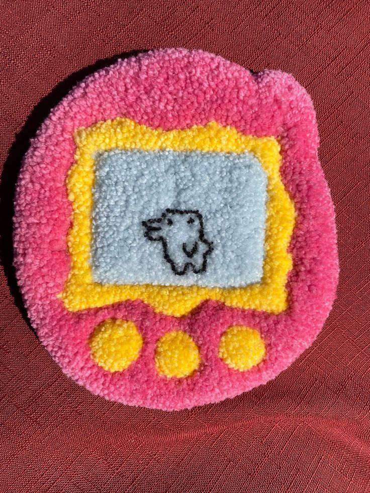 a small pink and yellow object with a sheep on it's face in front of a red background