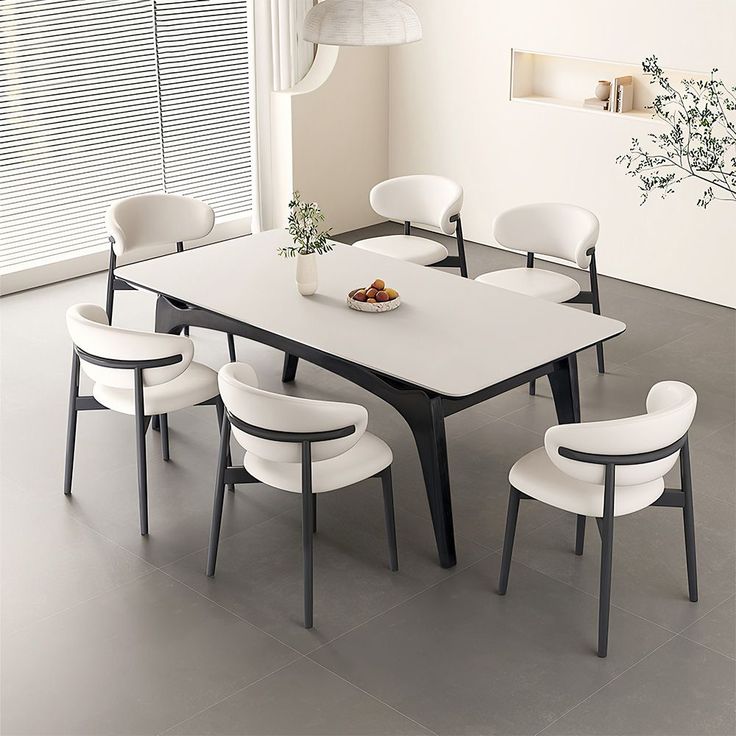 a dining table with six chairs and a bowl of fruit on it in front of a window