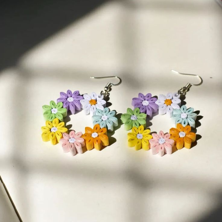 two pairs of earrings with flowers on them sitting on top of a white table next to a window