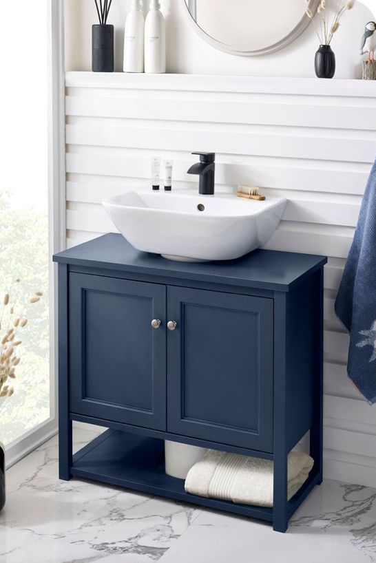 a white sink sitting under a mirror next to a blue cabinet