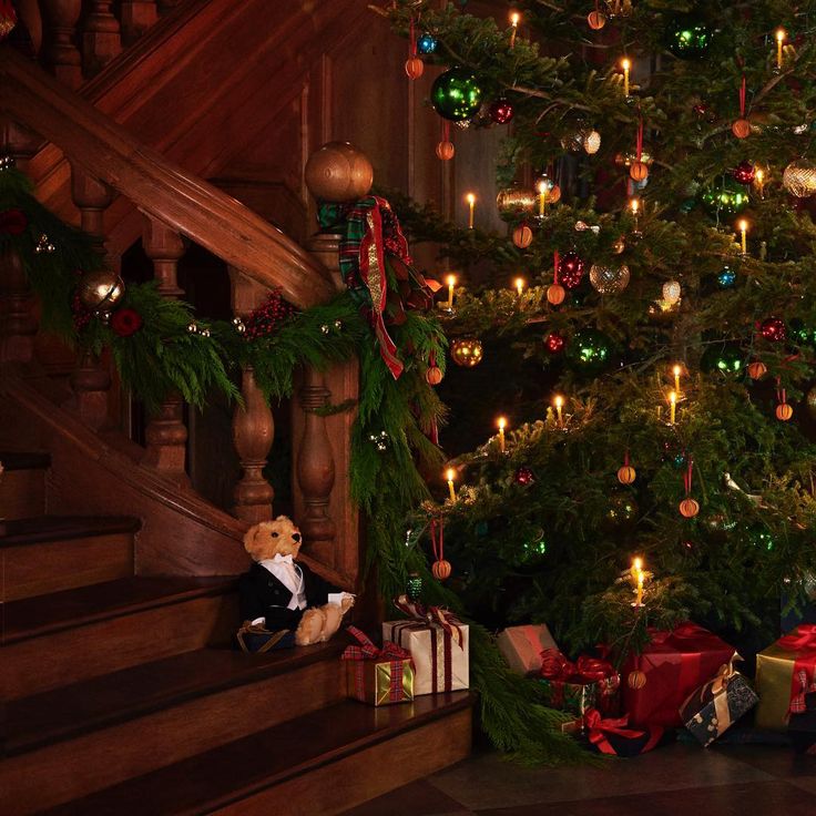 a teddy bear sitting on the stairs next to a christmas tree with presents under it