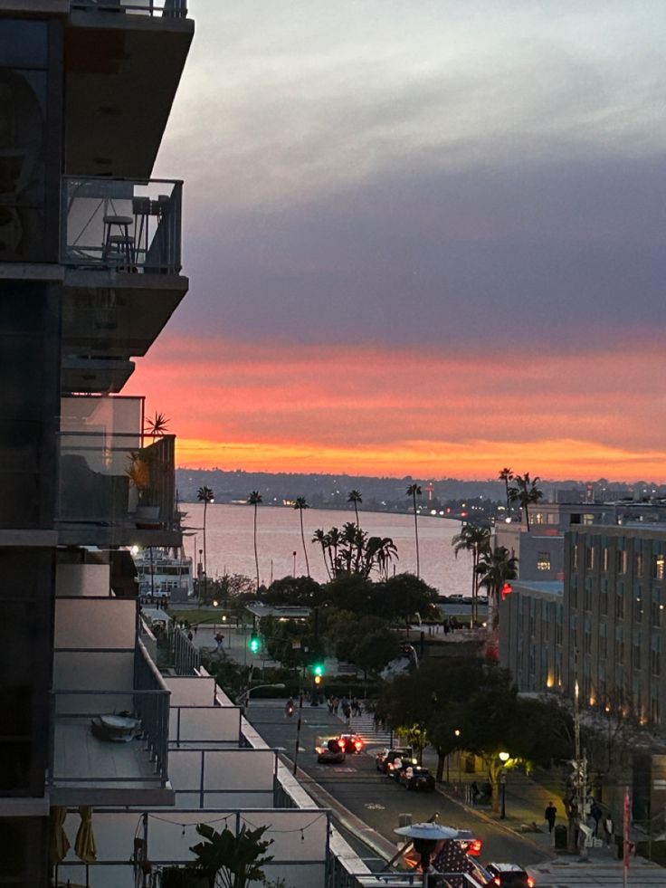 the sun is setting over an ocean and cityscape with cars parked on the street