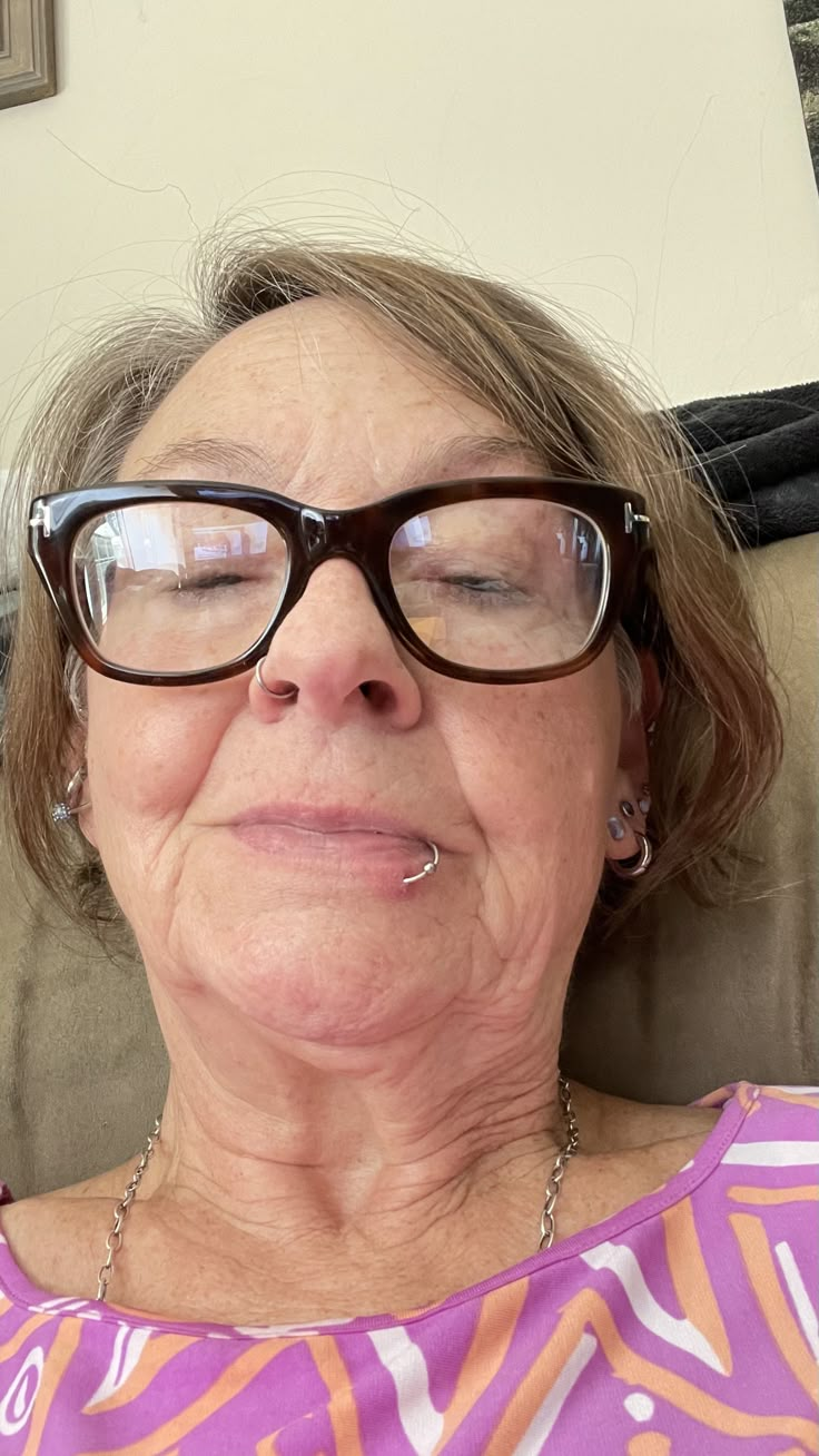 an older woman wearing glasses laying on a couch with her eyes closed and tongue out