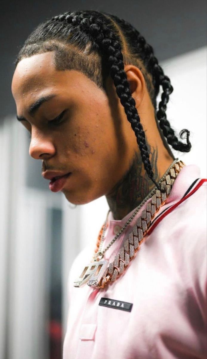 a man with long braids and a pink shirt is looking down at his cell phone