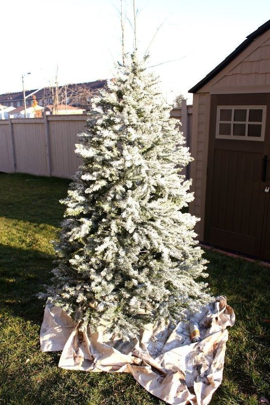 a white christmas tree is sitting in the grass next to a shed and some tarps