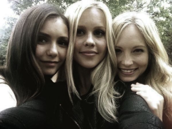 three beautiful young women standing next to each other in front of some trees and bushes