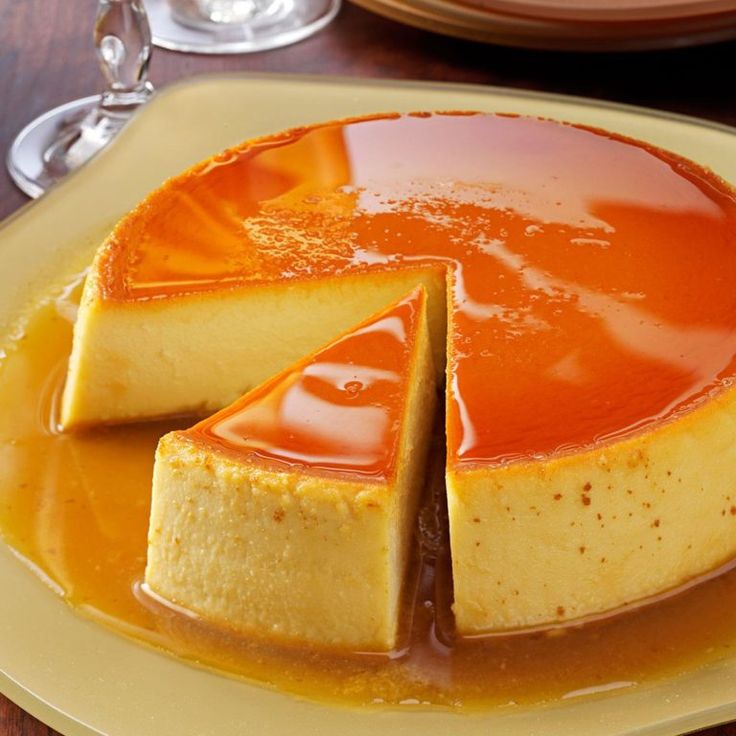 a cheesecake covered in caramel sauce on a yellow plate next to wine glasses