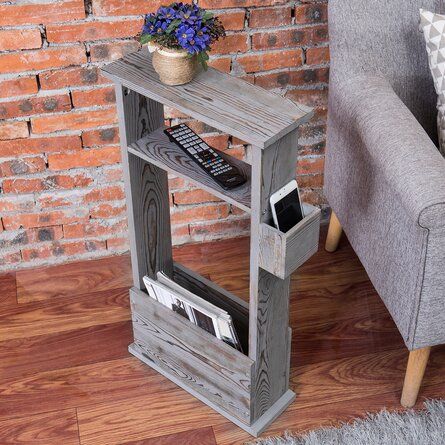 a grey chair sitting in front of a brick wall next to a wooden shelf with magazines on it