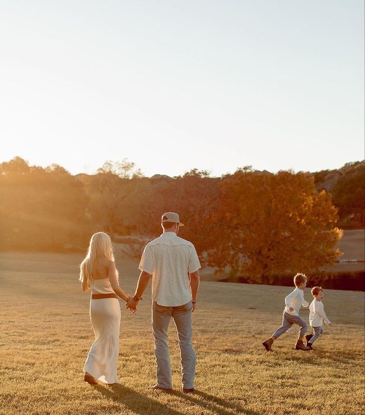 a man and woman holding hands while walking in the grass with two children behind them