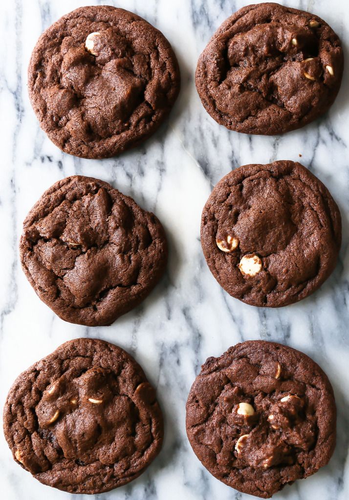 six chocolate cookies on a marble surface with walnuts in the middle and one half eaten