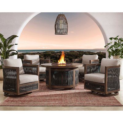 an outdoor fire pit surrounded by wicker chairs and tables with a view of the ocean