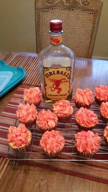 cupcakes with pink frosting are on a cooling rack next to a bottle of alcohol