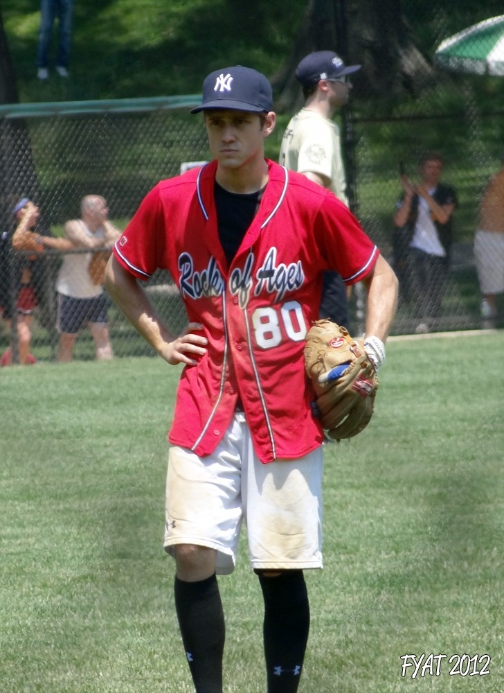 a baseball player standing in the grass with his mitt on and other players behind him