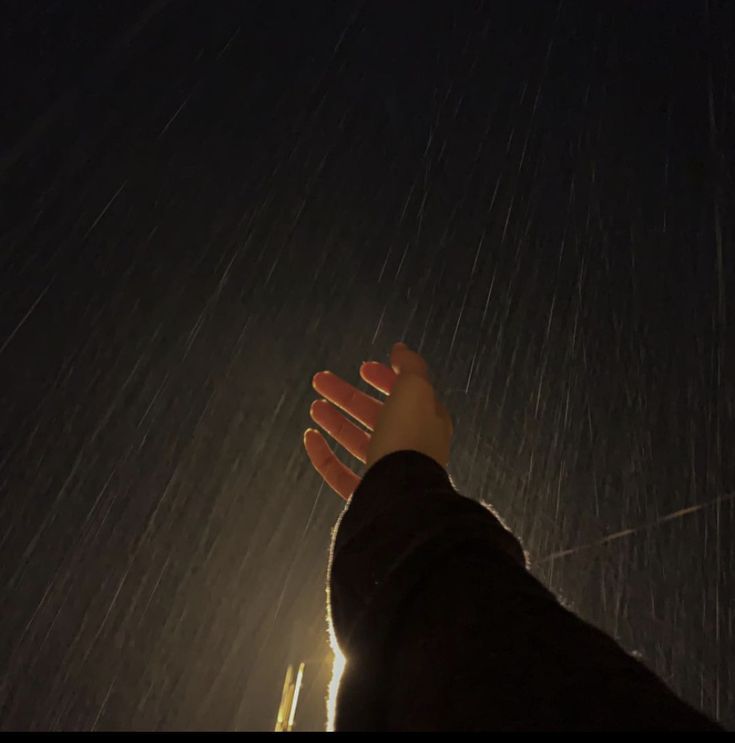 a person's hand reaching up into the sky with rain coming down on them