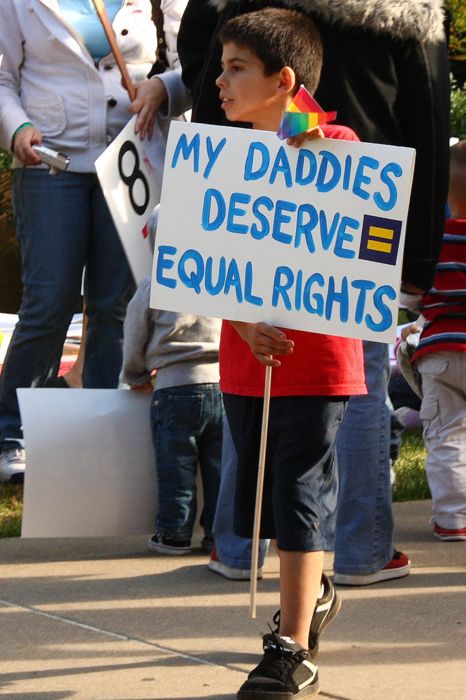 a young boy holding a sign that says my daddies deserves equal rights