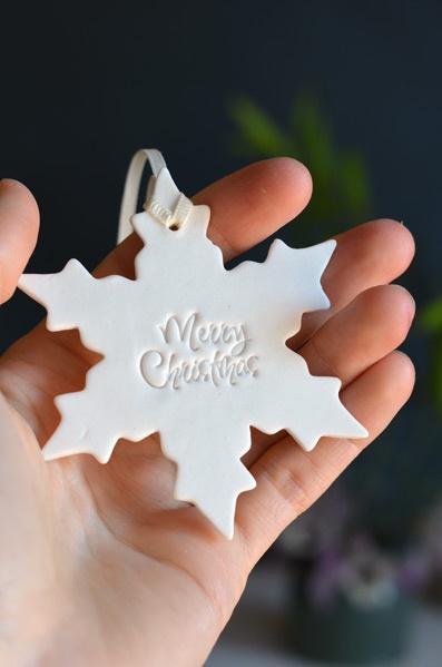 a hand holding a white ornament with the word merry christmas written on it