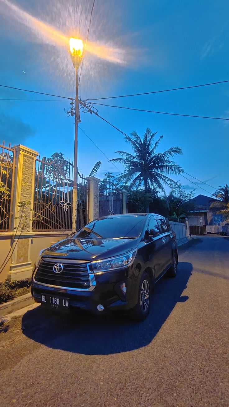 a car parked on the side of a road next to a street light and palm trees