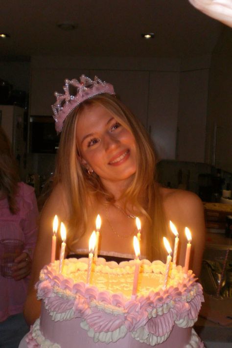 a woman wearing a tiara standing in front of a cake with lit candles