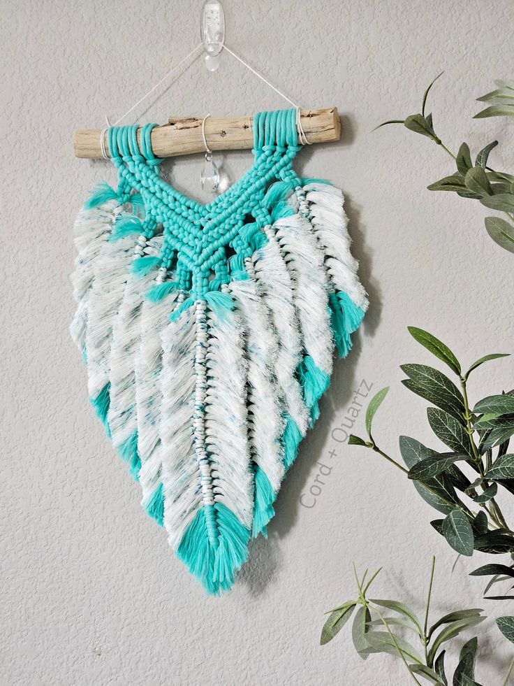 a blue and white crochet hanging on a wall next to a potted plant