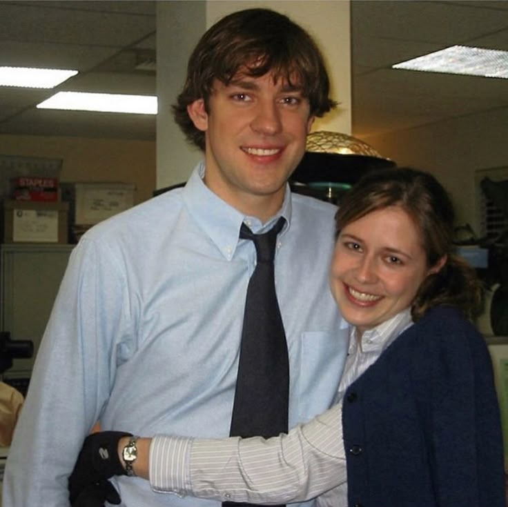 a man and woman posing for the camera in an office setting with their arms around each other