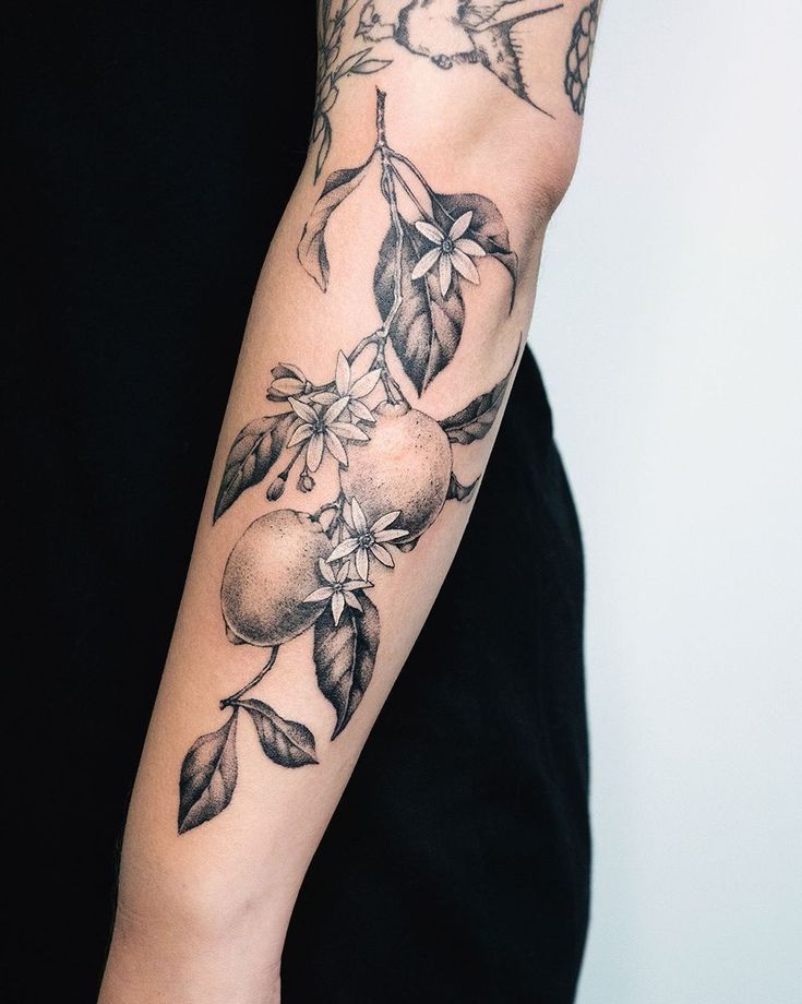 a person with a tattoo on their arm holding an apple and flower branch in front of them