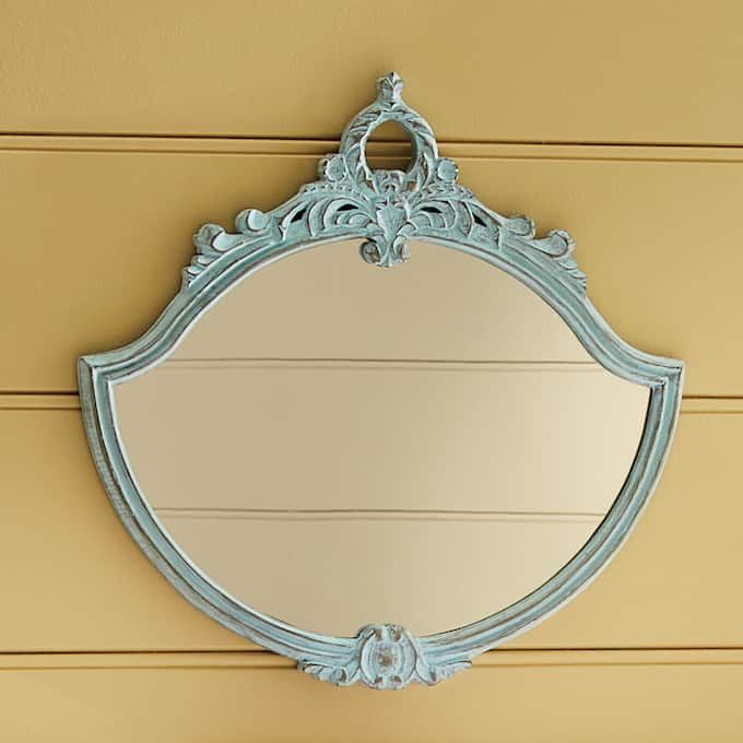 a mirror hanging on the side of a yellow wall next to a wooden paneled door