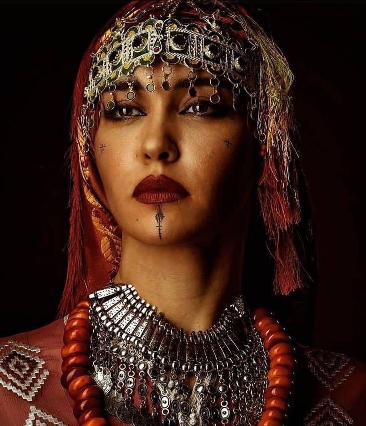 a woman with red hair and jewelry on her face, wearing an elaborate headdress