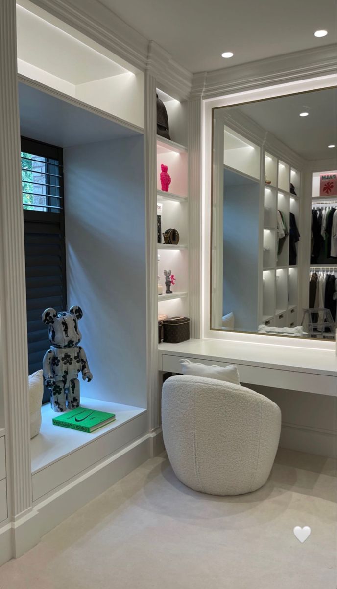 a teddy bear sitting on a stool in front of a large mirror and shelves with clothes