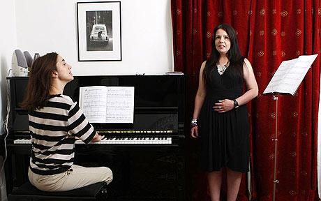 a woman standing next to a piano in front of a man sitting on the floor