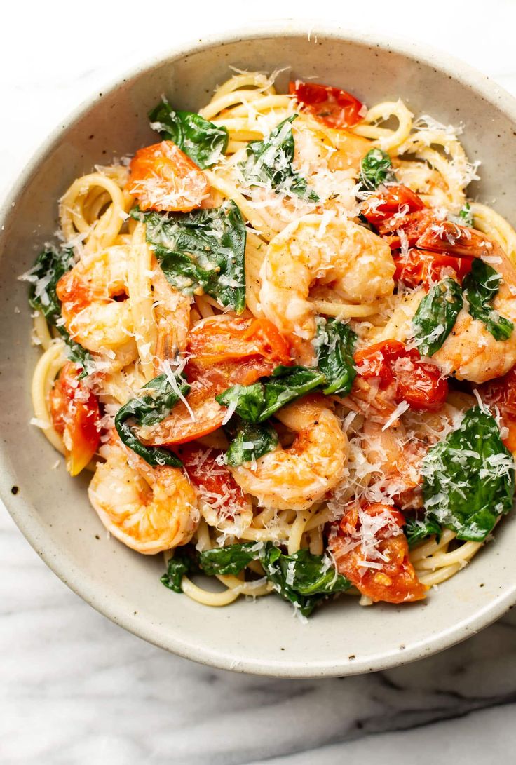 pasta with shrimp, spinach and tomato sauce in a white bowl on a marble surface