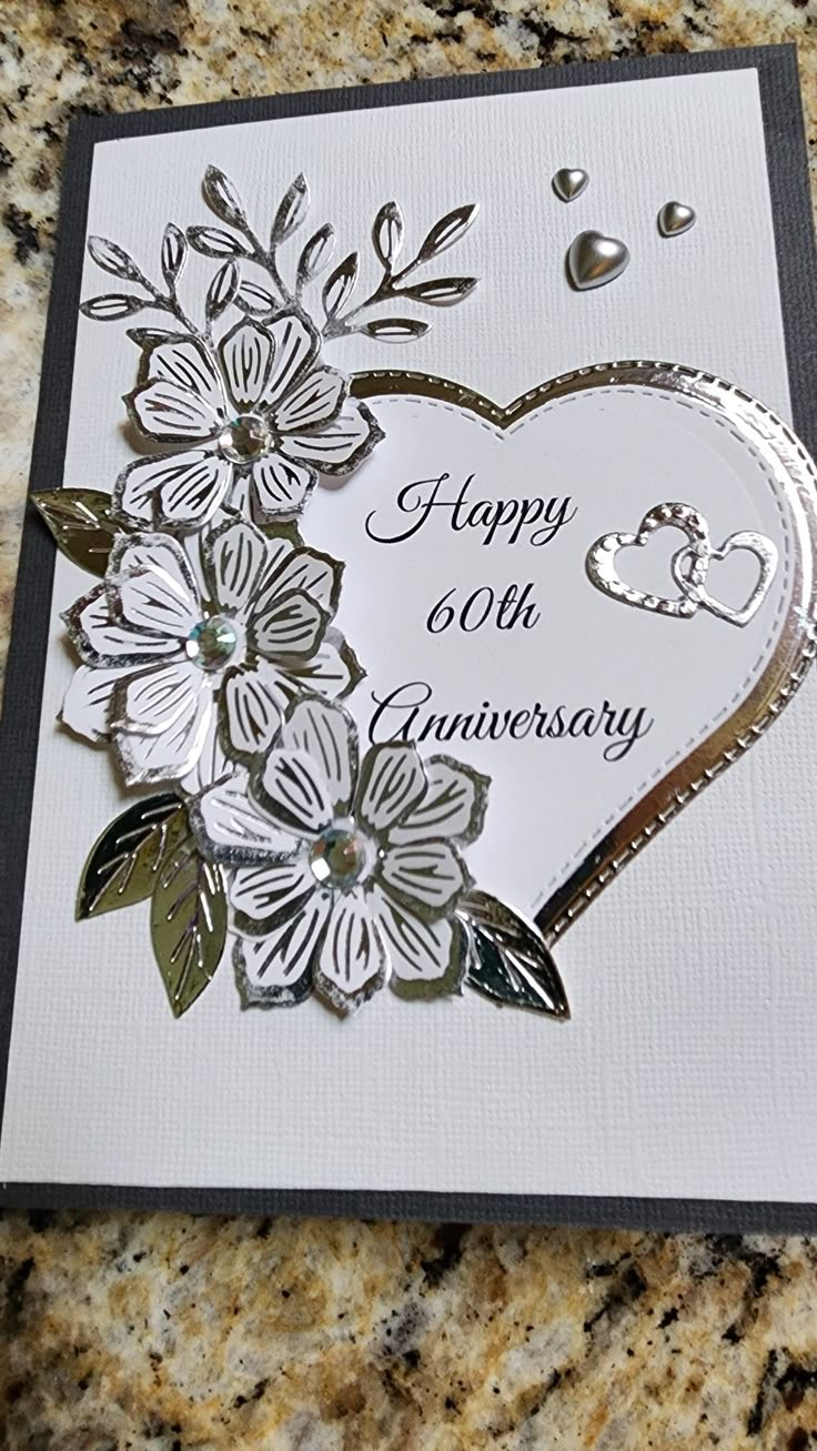 a white and silver anniversary card with flowers on the front, surrounded by other greeting cards