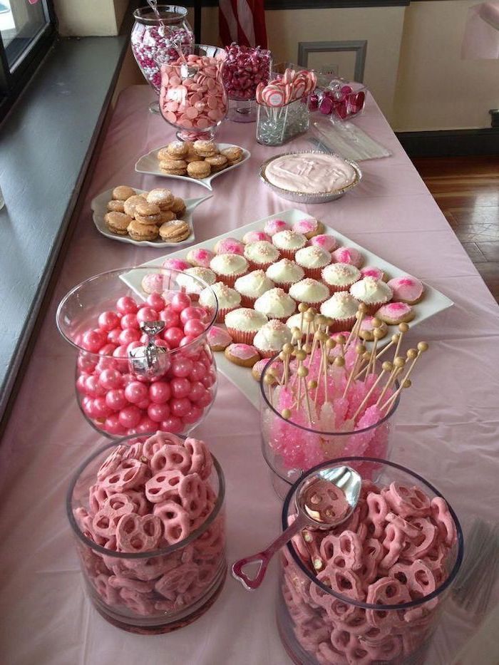 the table is set up with pink and white desserts, cupcakes, and candy