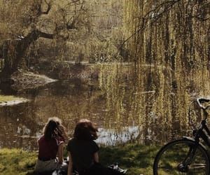 two people sitting on the grass near a pond and bike in the background, with trees reflected in the water