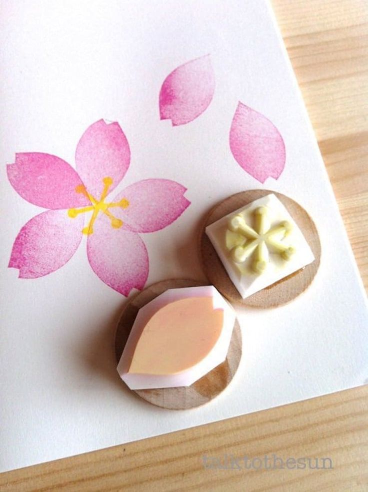 some pink flowers and two wax blocks on a white paper with watercolors in the background