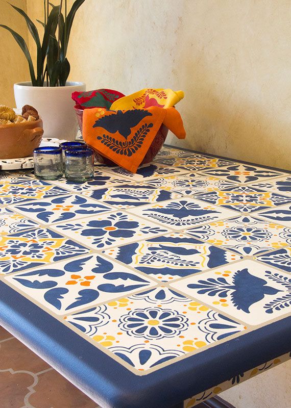 a blue and yellow patterned table cloth on top of a wooden table with potted plants in the background