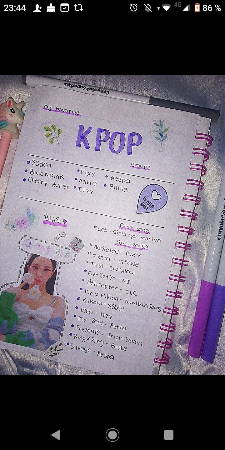 an open notebook with pictures on it and a pen sitting next to the page that says kpop