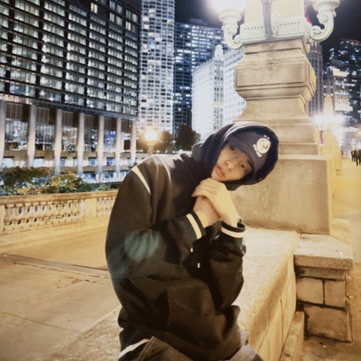 a young man in a hoodie is leaning against a stone wall with his hands on his chin