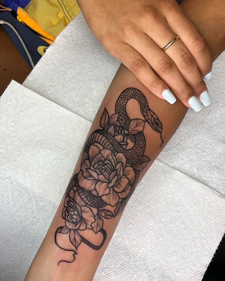 a woman's arm with a snake and roses tattoo on the left side of her arm