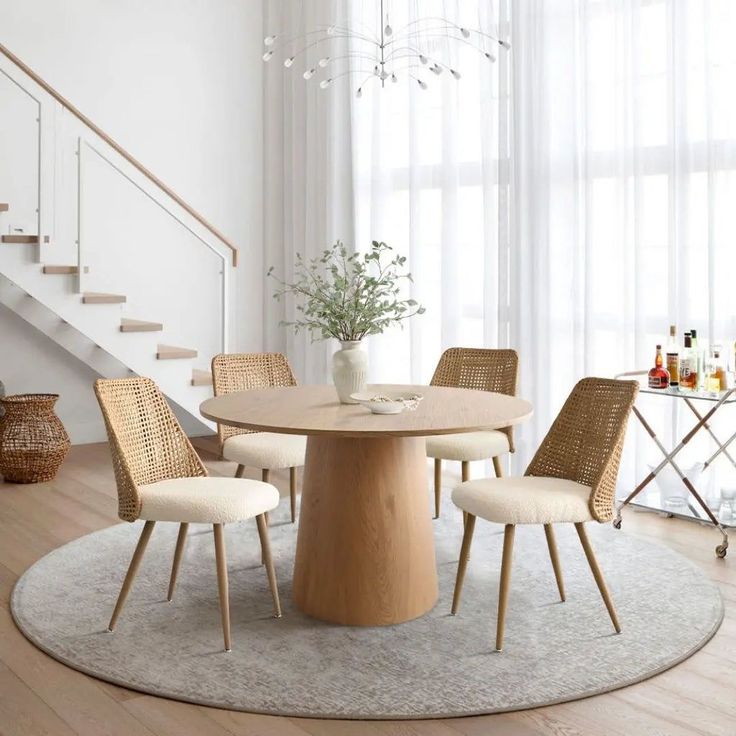 a round table with four chairs around it in front of a stair case and window