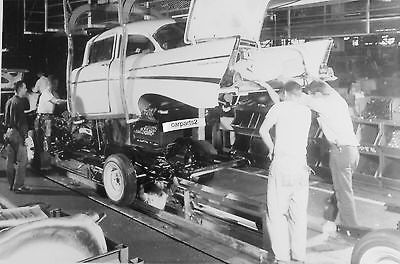 an old black and white photo of men working on a car in a factory with other people standing around