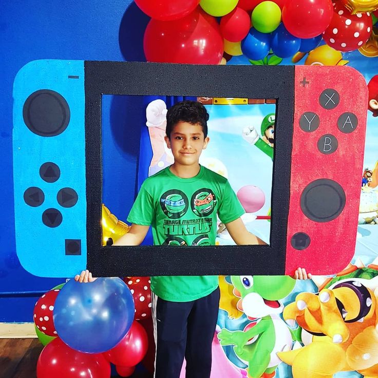 a young boy holding up a nintendo wii game controller in front of balloons and streamers